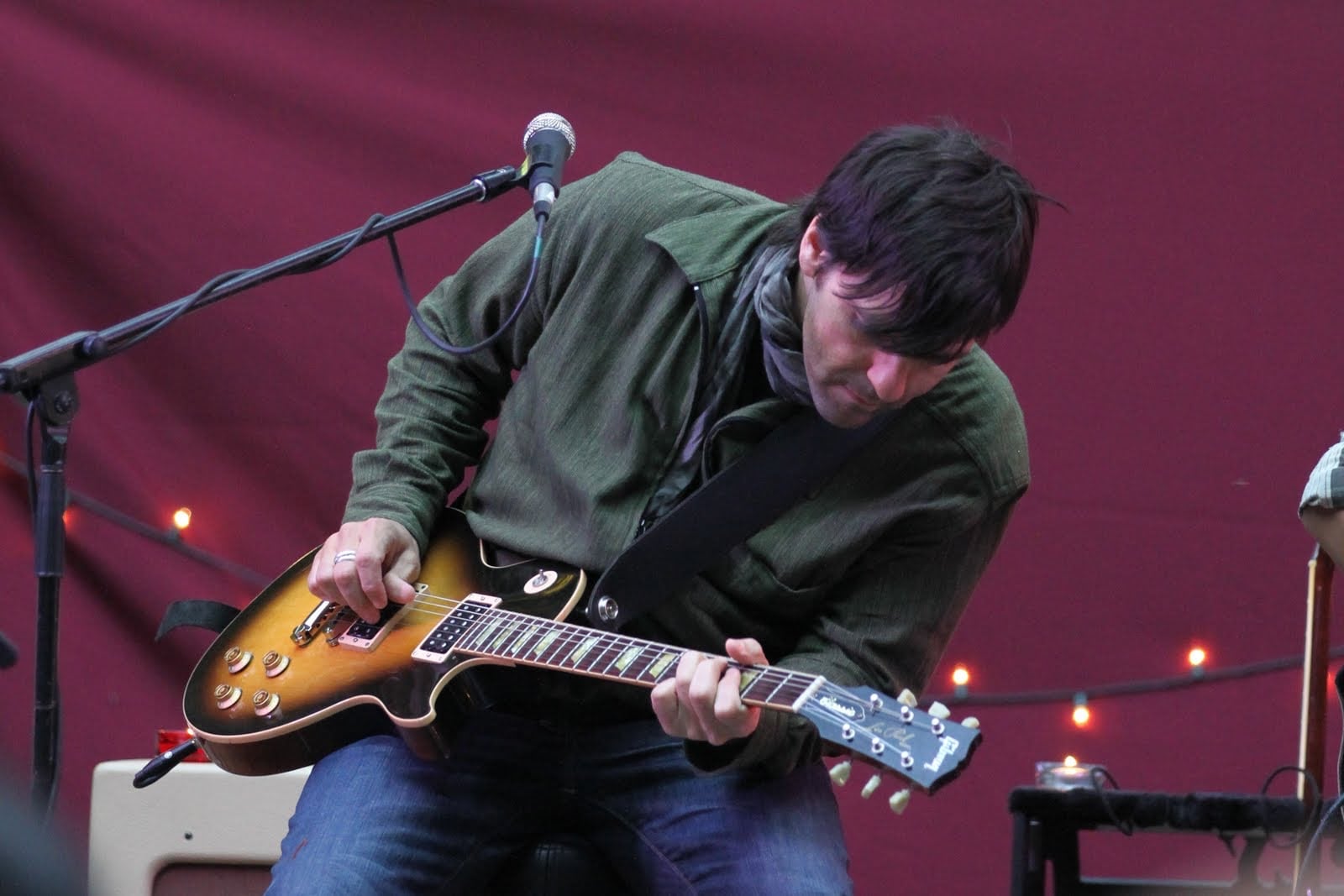 Nathan Dale leaning into an electric guitar performance against a deep red stage backdrop in Big Sur
