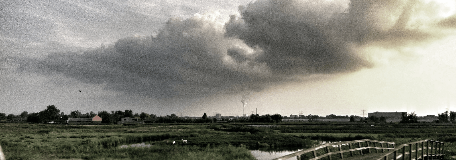 Storm clouds advancing over fields and an industrial horizon